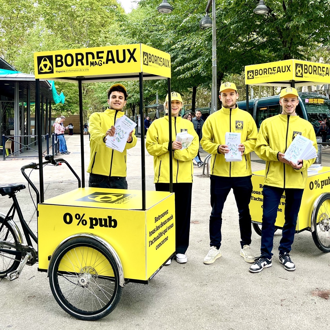 Les équipes Velo Expo pour la Mairie de Bordeaux. Distribution à vélo de Bordeaux Mag, le magazine de la Ville de Bordeaux. Photo prise place de la Comédie à Bordeaux. Campagne communication ooh hors-media par activation affichage mobile avec vélo triporteur publicitaire street marketing | Velo Expo | Agence Veymont