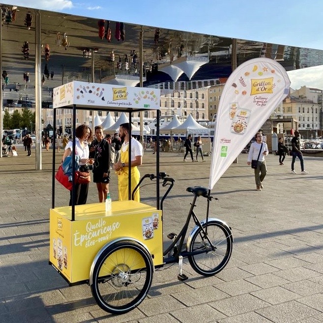 Velo Expo pour Grillon d'Or, à Marseille Vieux Port. Animation, distribution, échantillonnage et dégustation avec vélo triporteur personnalisé et oriflamme publicitaire. Campagne communication ooh hors-media par activation affichage mobile avec vélo triporteur publicitaire street marketing | Velo Expo | Agence Veymont