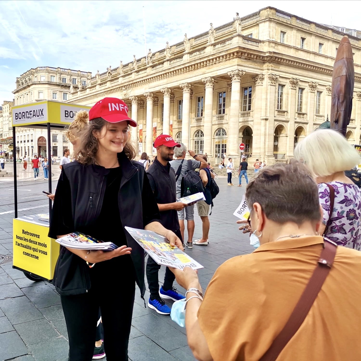 Les équipes Velo Expo pour la Mairie de Bordeaux. Distribution à vélo de Bordeaux Mag, le magazine de la Ville de Bordeaux. Photo prise place de la Comédie à Bordeaux. Campagne communication ooh hors-media par activation affichage mobile avec vélo triporteur publicitaire street marketing | Velo Expo | Agence Veymont