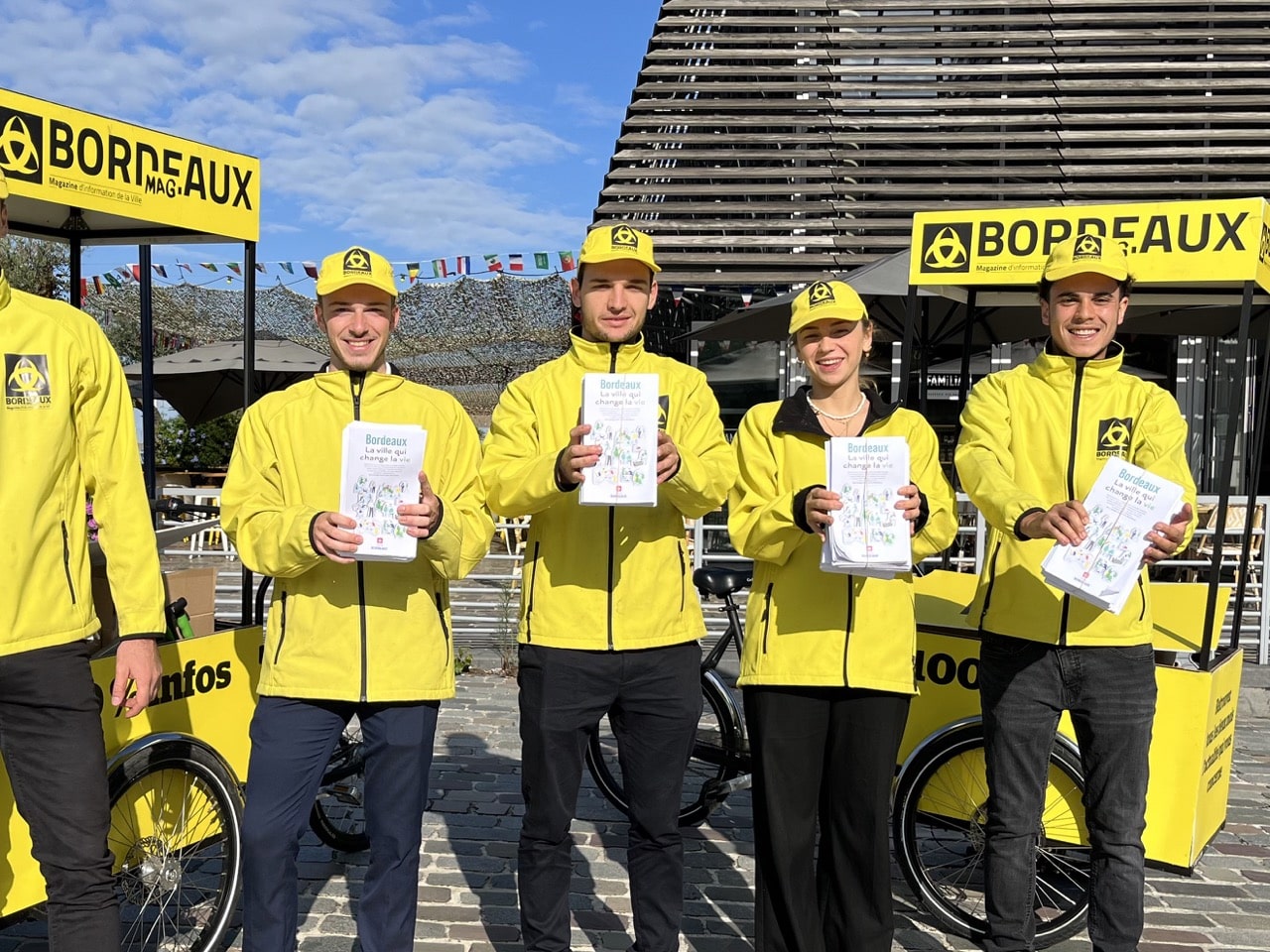 Les équipes Velo Expo pour la Mairie de Bordeaux. Distribution à vélo de Bordeaux Mag, le magazine de la Ville de Bordeaux. Photo prise place de la Comédie à Bordeaux. Campagne communication ooh hors-media par activation affichage mobile avec vélo triporteur publicitaire street marketing | Velo Expo | Agence Veymont