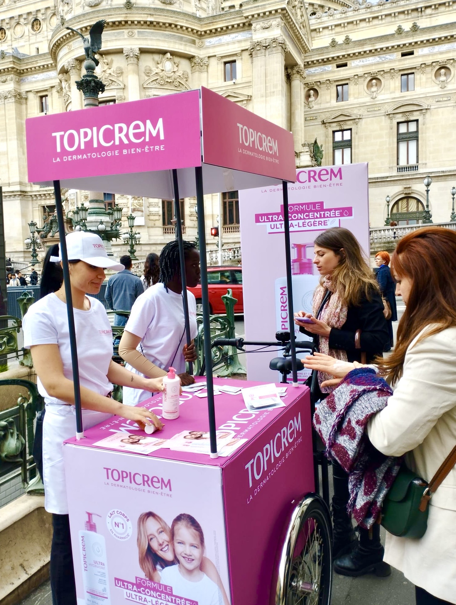 Velo Expo pour Topicrem place de l'Opéra à Paris France. Animation, distribution et échantillonnage avec vélo affichage mobile grand format. Campagne communication ooh hors-media par activation affichage mobile digital avec vélo triporteur publicitaire street marketing | Velo Expo | Agence Veymont