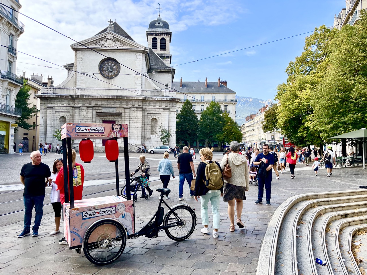 Place Saint André. Grenoble. Velo Expo KI-00N. Campagne de communication et promotion de Akane-banashi par la distribution d'échantillons avec vélo publicitaire triporteur personnalisés. Campagne communication ooh hors-media par activation affichage mobile digital avec vélo triporteur publicitaire street marketing | Velo Expo | Agence Veymont