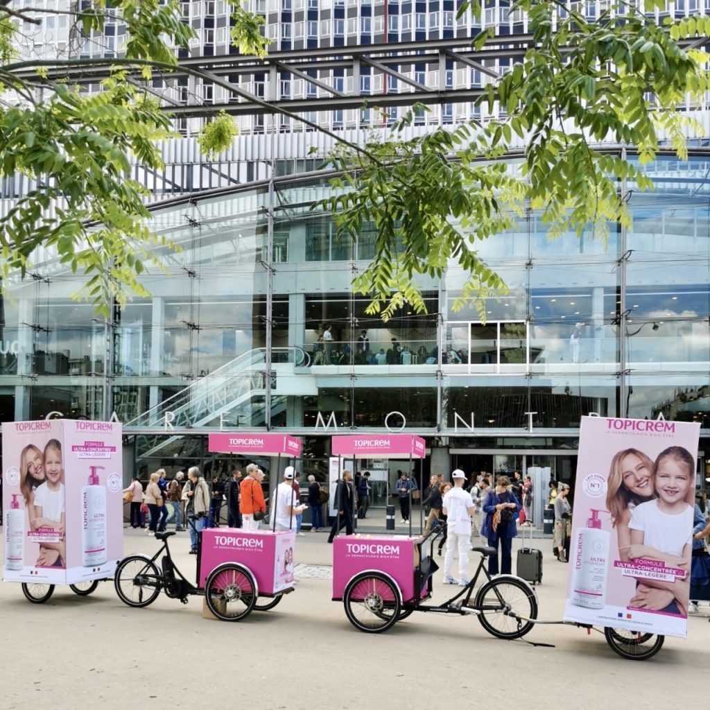 Velo Expo pour Topicrem gare Montparnasse à Paris France. Animation, distribution et échantillonnage avec vélo affichage mobile grand format. Campagne communication ooh hors-media par activation affichage mobile digital avec vélo triporteur publicitaire street marketing | Velo Expo | Agence Veymont