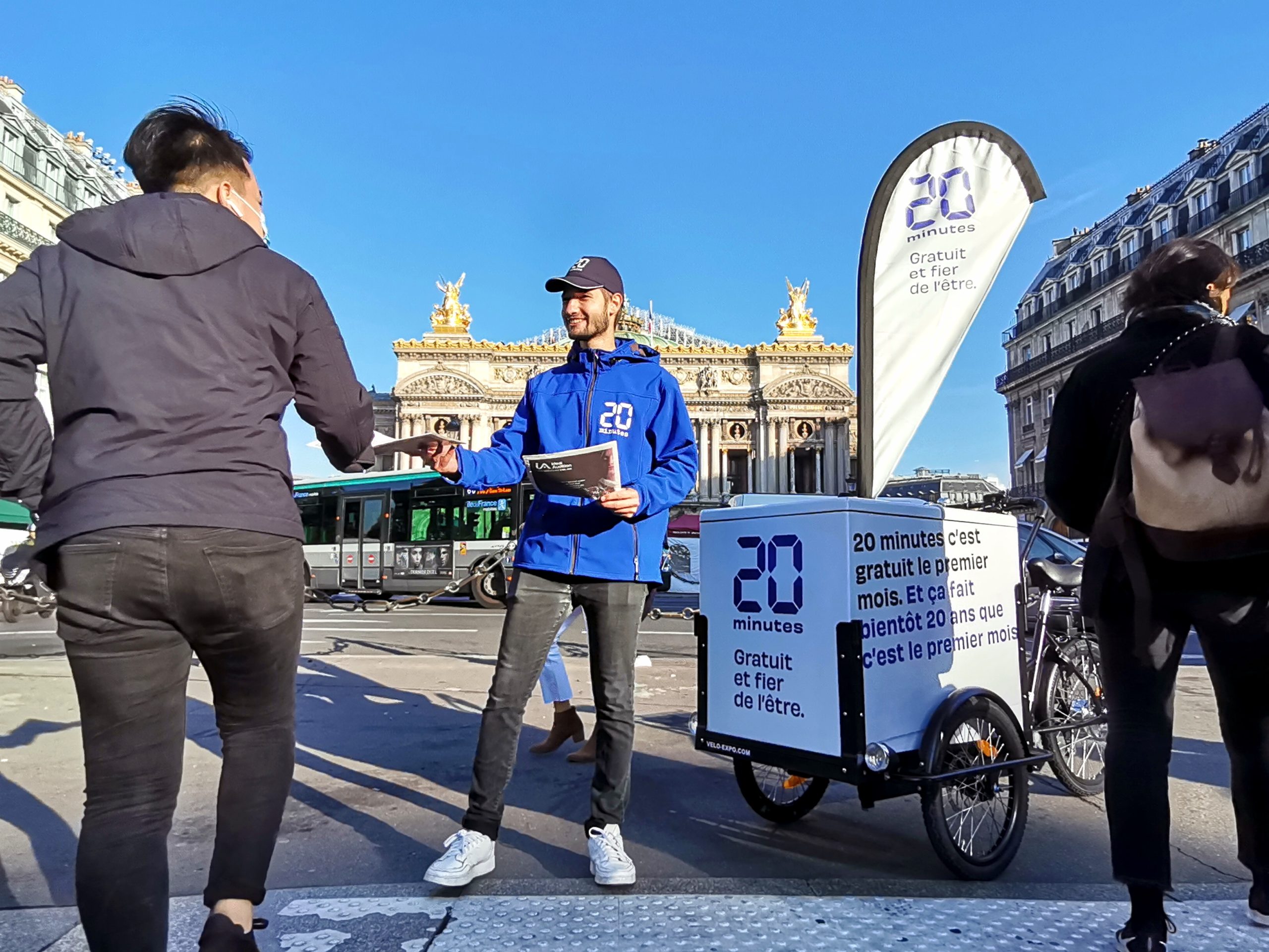 Velo Expo pour le journal 20 Minutes. Distribution à vélo du journal 20 Minutes. Campagne communication ooh hors-media par activation affichage mobile digital avec vélo triporteur publicitaire street marketing | Velo Expo | Agence Veymont